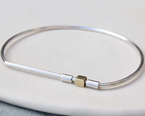 A silver bar bangle bracelet with a brass spinner section, displayed on a white surface.
