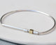 A silver bar bangle bracelet with a brass spinner section, displayed on a white surface.