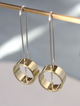 A pair of gold-colored brass circle spinner earrings hanging from a silver wire on a display stand.