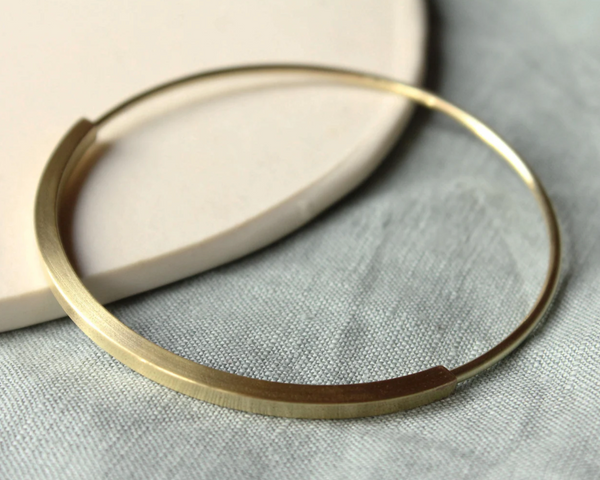 A gold-colored brass tube spinner bangle bracelet placed on a white surface.