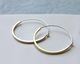 A pair of silver and gold tube hoop earrings placed against a light background.