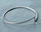 Silver bangle with a triangle charm on a gray fabric background