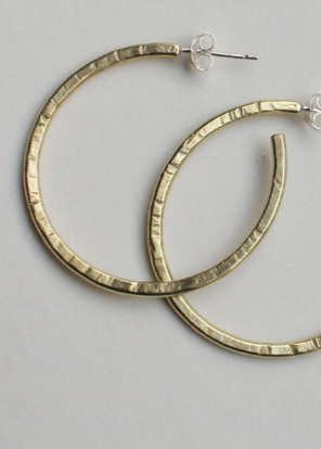 A pair of gold-colored hammered brass hoop earrings laid on a flat surface.