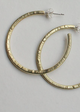 A pair of gold-colored hammered brass hoop earrings laid on a flat surface.