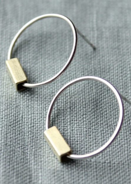 Silver hoop earrings with gold rectangular accents on a gray fabric background
