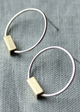Silver hoop earrings with gold rectangular accents on a gray fabric background