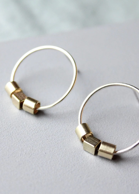 A pair of hoop earrings with geometric studs attached to the hoop, displayed against a grey background.