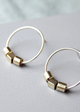 A pair of hoop earrings with geometric studs attached to the hoop, displayed against a grey background.