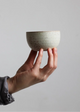 Hand holding a small ceramic bowl against a plain background