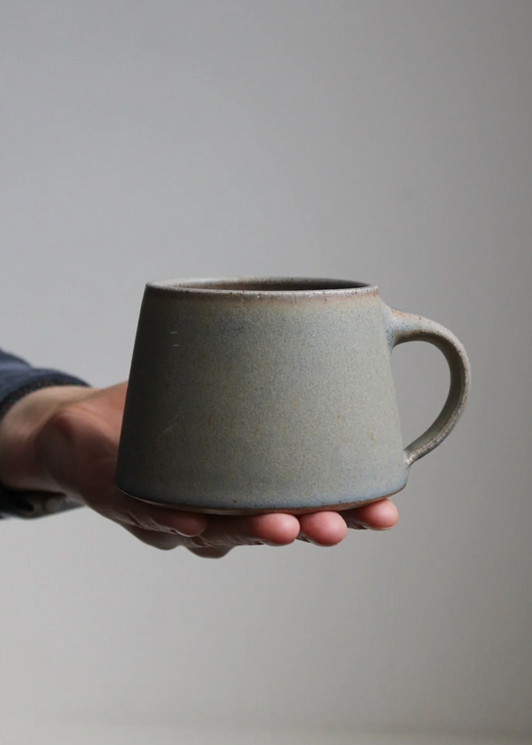 Hand holding a gray ceramic mug against a plain background