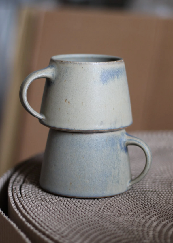 Two stacked ceramic mugs on a textured surface with a blurred background