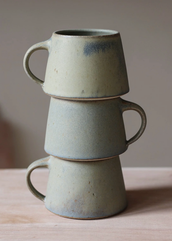 Stack of three ceramic mugs on a wooden surface with a neutral background