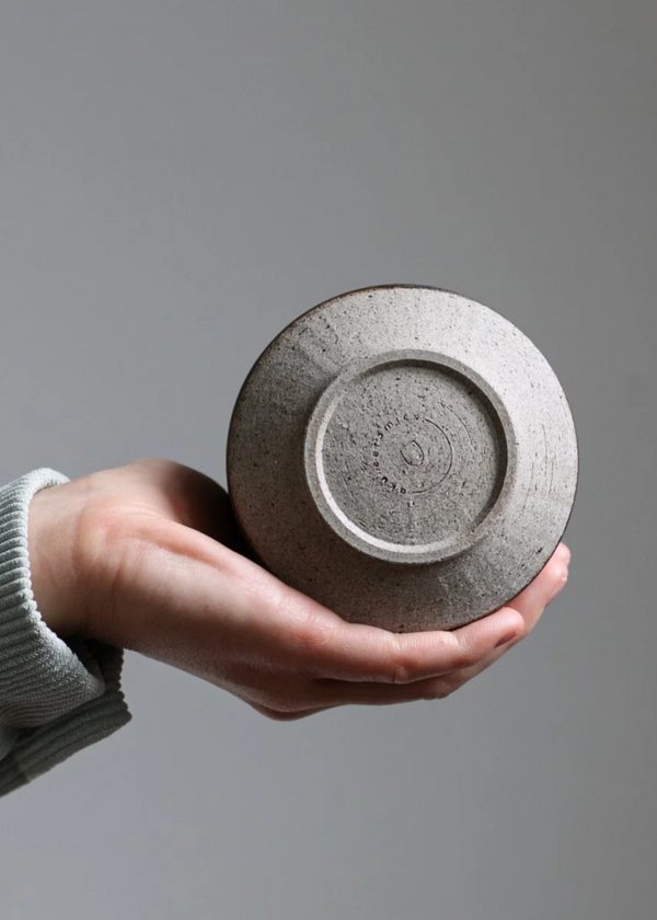 Hand holding a textured ceramic plate against a gray background