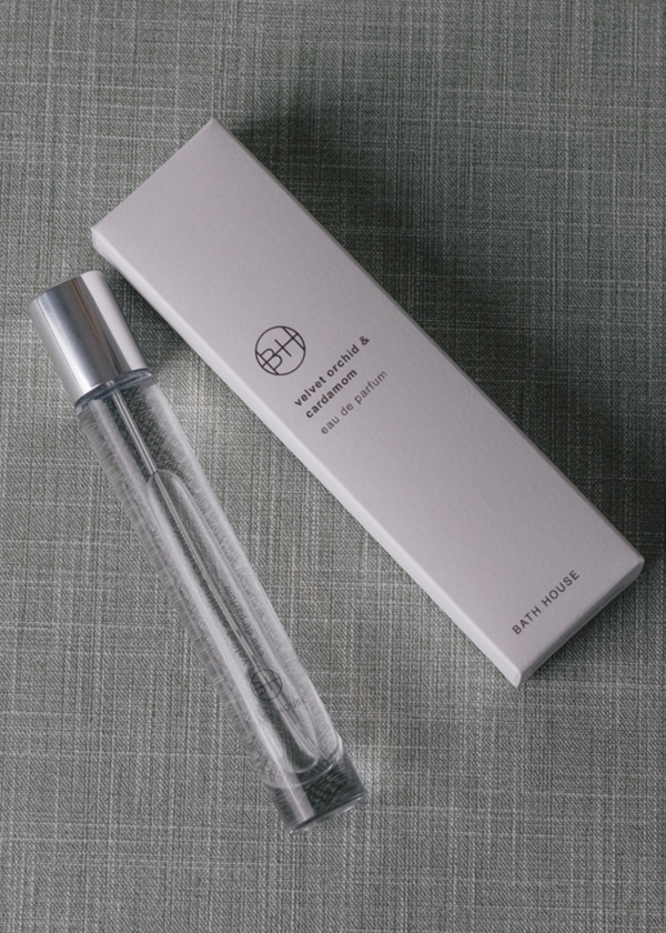 Clear glass bottle of perfume with silver cap and white box on a textured gray background