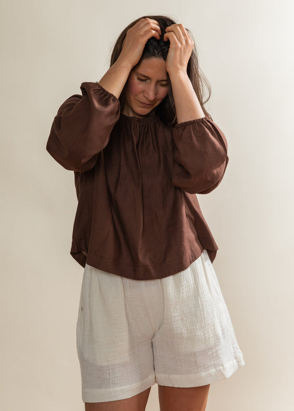 Woman wearing a brown blouse and white shorts against a plain background