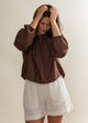 Woman wearing a brown blouse and white shorts against a plain background