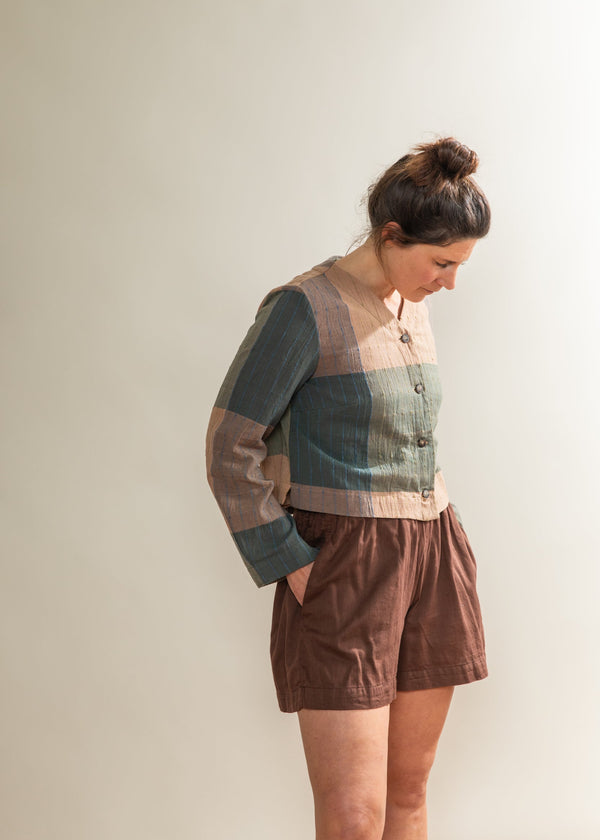 Woman wearing a patchwork shirt and brown shorts against a plain background