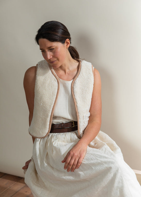 Woman wearing a white sleeveless garment and skirt against a plain background