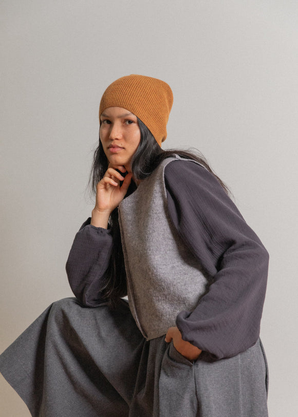 Person wearing a orange beanie and gray outfit against a plain background