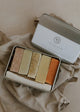 Five soap bars in a metal tin with a branded lid on a beige fabric background