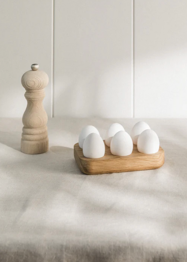 A wooden egg holder filled with eggs, placed on a table with a wooden salt shaker in the background.