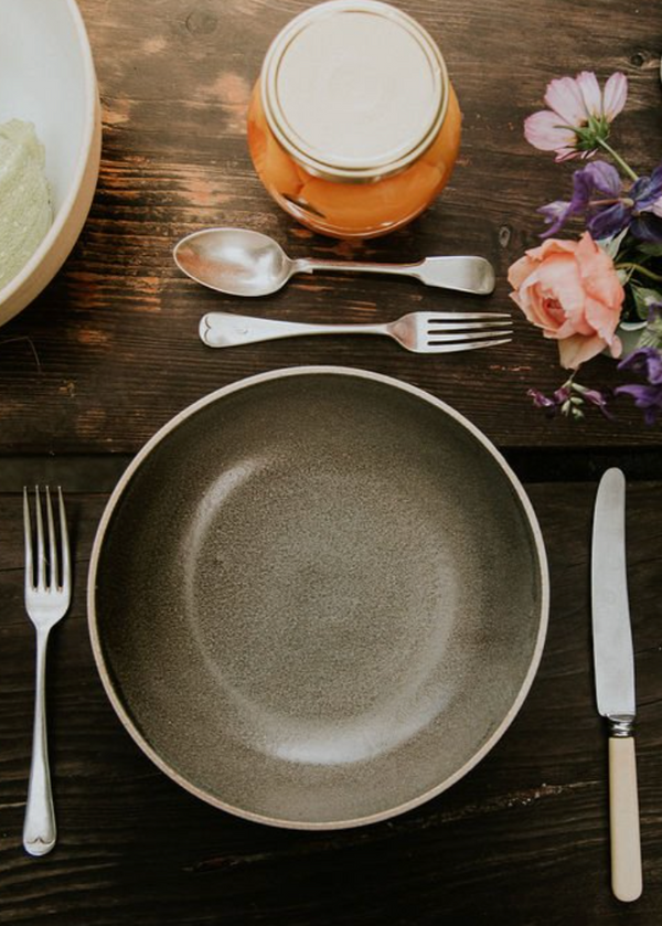Dining table setting with plates, cutlery, and decorative flowers on a wooden surface.
