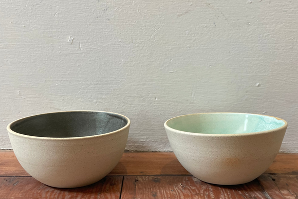 Two ceramic bowls side by side, one with a green interior and one with a black interior, both with beige exteriors and placed against a neutral background.