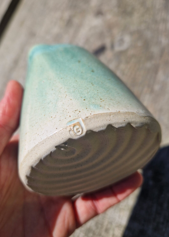 Hand holding a ceramic cone with a brand logo on a concrete surface