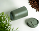 Green travel mug with lid on a white surface with coffee beans and a plant.
