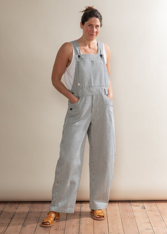 Person wearing light blue denim overalls standing against a plain background