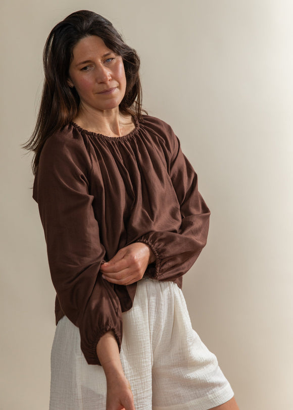 Woman wearing a brown blouse and white pants against a plain background