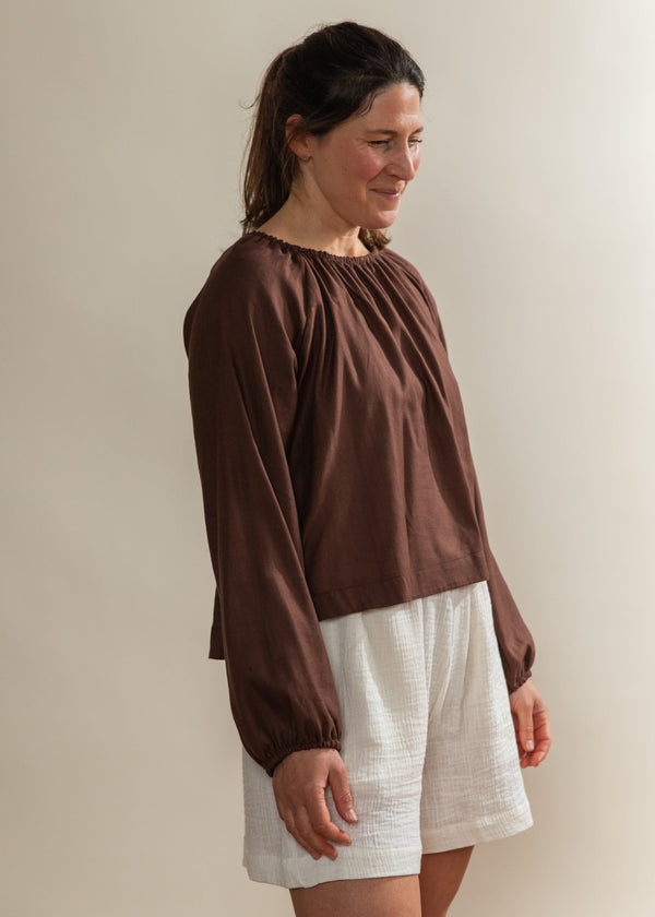 Woman wearing a brown top and white shorts against a plain background