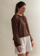 Woman wearing a brown top and white shorts against a plain background