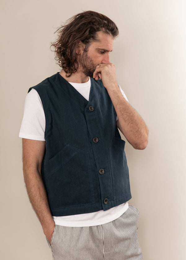 Man wearing a dark green vest over a white shirt with a beige background