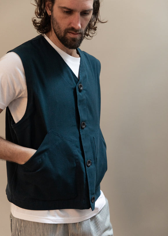 Man wearing a dark green vest over a white shirt with a neutral background