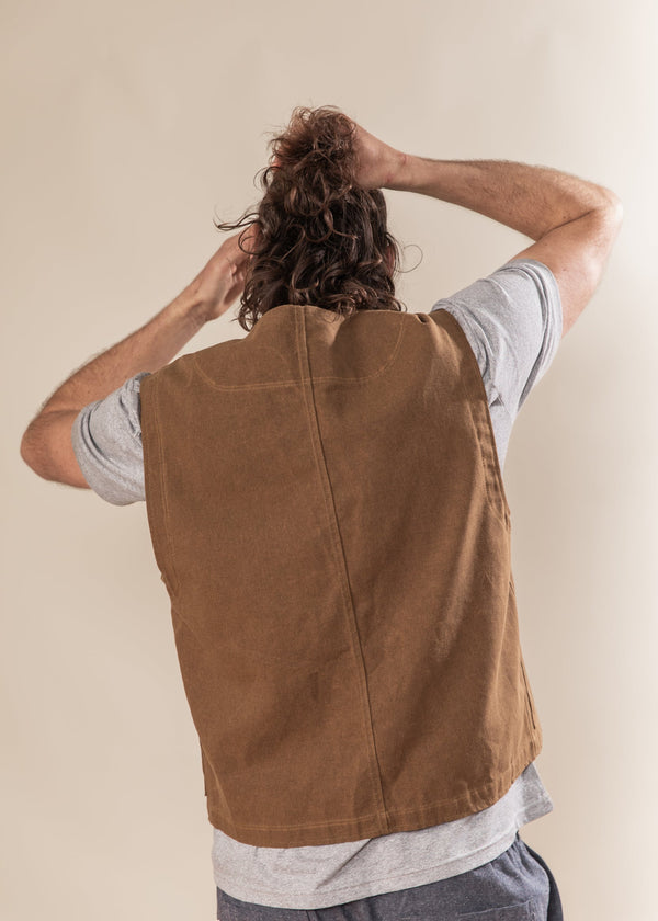 Person wearing a brown vest over a gray shirt with a plain background