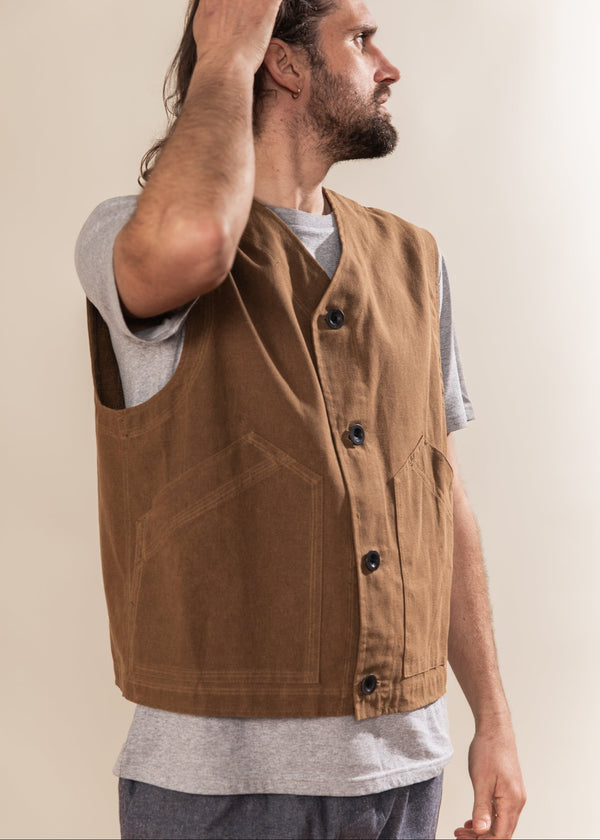 Man wearing a brown vest over a gray shirt against a beige background