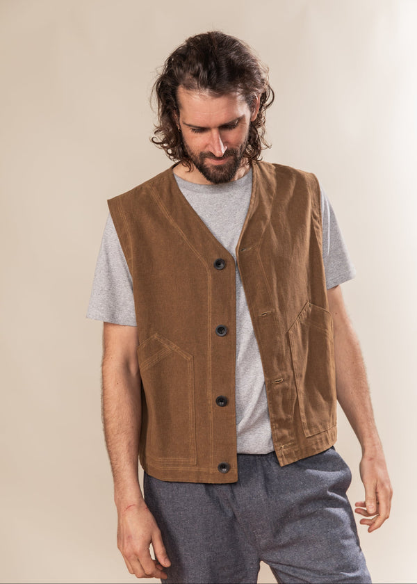 Man wearing a brown vest over a gray shirt against a beige background