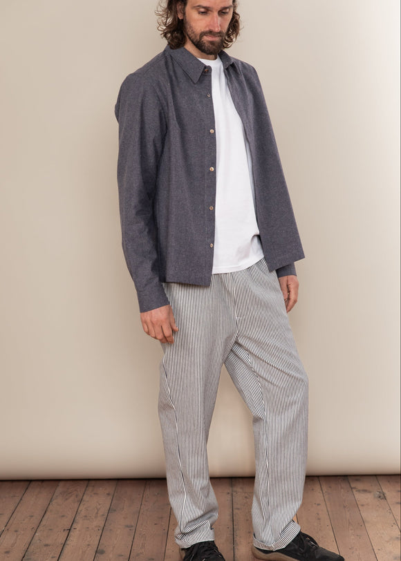 Man wearing a dark shirt over a white t-shirt with light gray pants on a wooden floor.