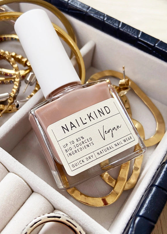 Nail polish bottle with 'NAILKIND' branding on a jewelry box with gold bracelets.
