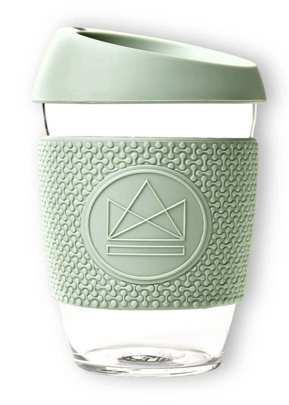 A clear glass coffee cup with a solid pattern, featuring a green lid and silicone sleeve, with the Neon Kactus logo on the sleeve.