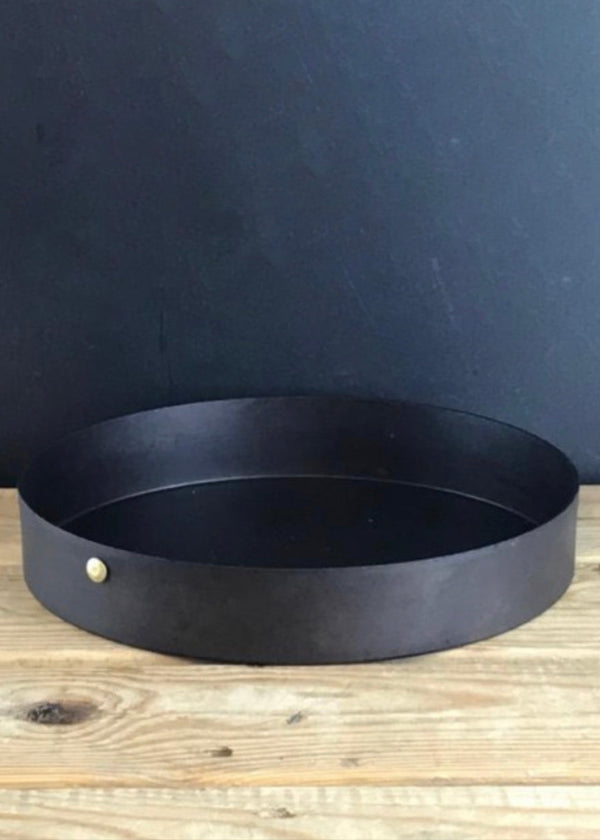 Black metal tray with a small gold knob on a wooden surface against a dark background