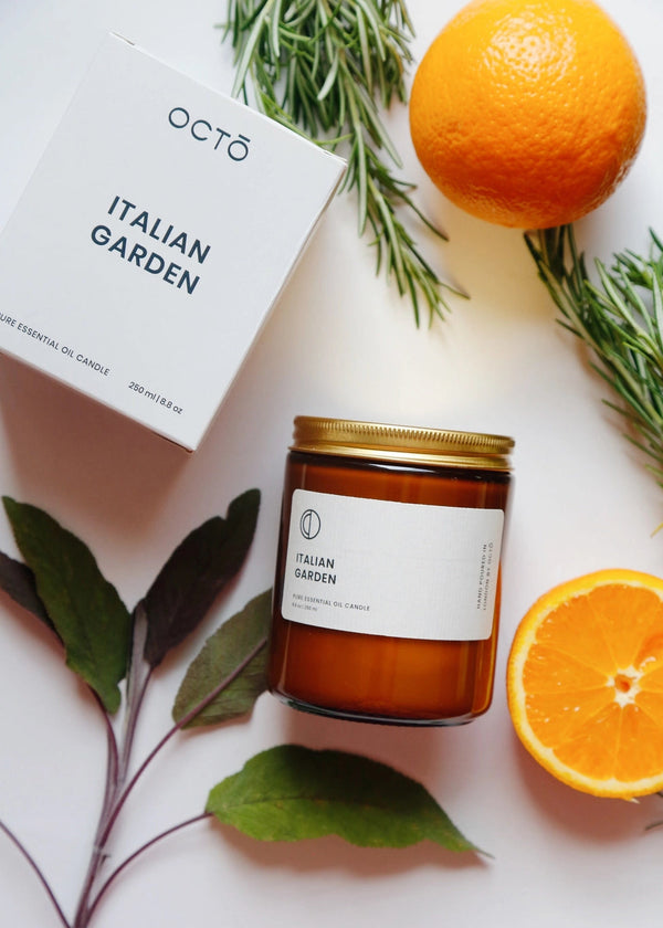 Candle labeled 'Italian Garden' with oranges and rosemary on a light surface