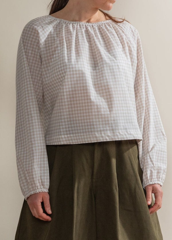 Person wearing a white checkered blouse and green skirt standing on a wooden floor.