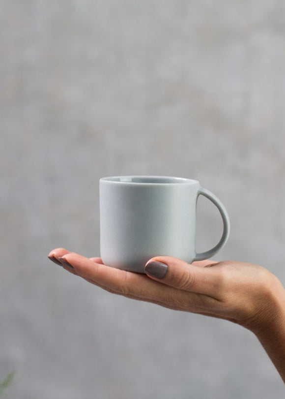 A person holding a plain grey porcelain mini mug with a handle.