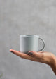 A person holding a plain grey porcelain mini mug with a handle.