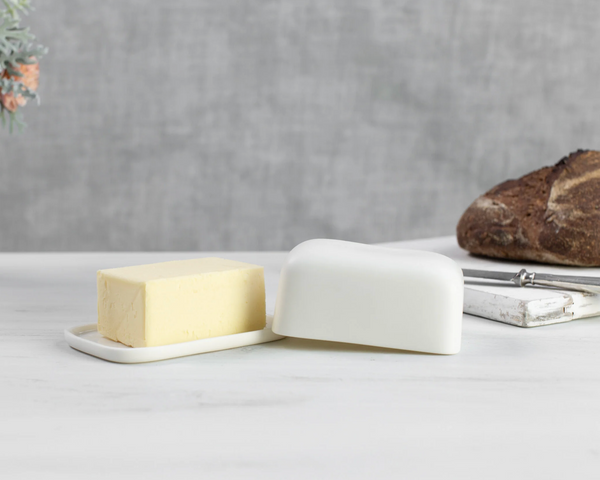 Butter dish with a stick of butter and a block of butter on a gray surface.