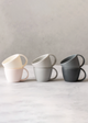 Three mugs in white, gray, and black on a marble surface with a neutral background