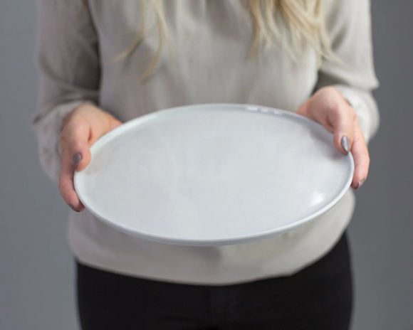 Person holding a white ceramic plate against a gray background
