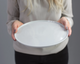 Person holding a white ceramic plate against a gray background